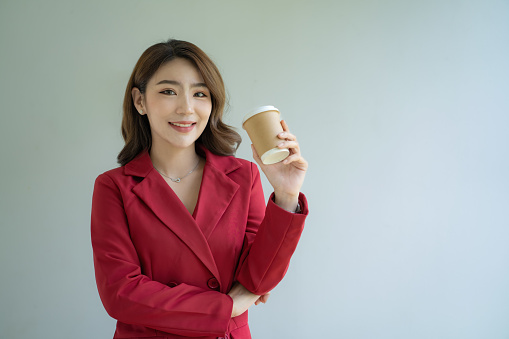 Asian businesswomen in red suits holding a cup of coffee over white background.