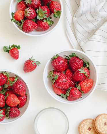 White bowls with fresh red strawberries, glass of milk and cookies. Healthy breakfast with berries. Top view.