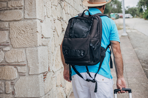 An old tourist carries a backpack and a suitcase