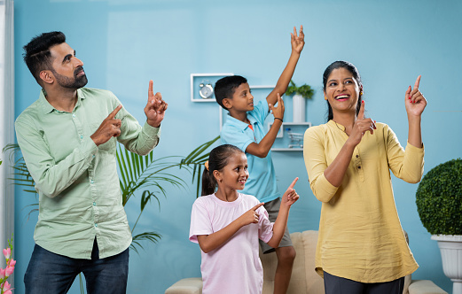 Cheerful Indian couple dancing with siblings kids at new home or apartment - concept of leisure activities, carefree living and holidays or vacation