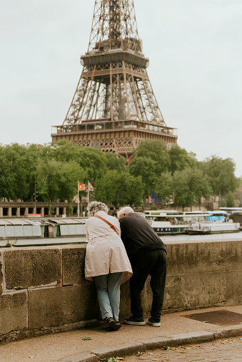 Paris, France - May 23, 2023: Elder couple back portrait resting while looking at Eiffel Tower. The Eiffel Tower (French: tour Eiffel) is a wrought-iron lattice tower on the Champ de Mars in Paris, France, and its tallest structure. It is named after the engineer Gustave Eiffel, whose company designed and built the tower. Locally nicknamed \