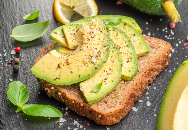 istock Avocado toast - bread with avocado slices on natural slate serving board. Top view. 1539348404
