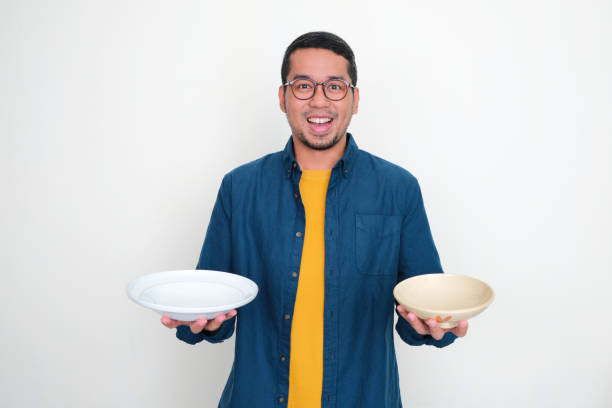 istock A man showing happy expression with one hand holding empty dinner plate and other hand holding empty bowl 1539350053