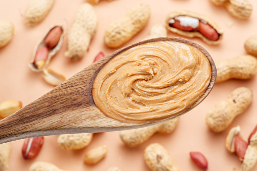 Wooden spoon with peanut butter. Peanuts lay on beige at the background. Top view.