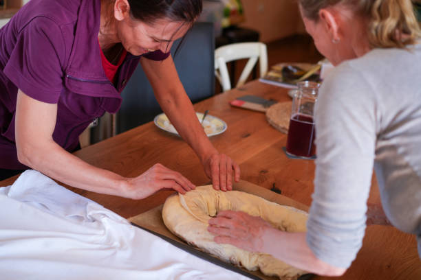 Two women fixing rolled strudel into pan for baking. stock photo