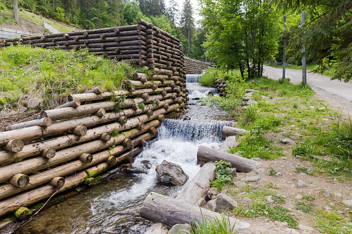 Mountain stream with artificial waterfalls and protect shoreline structure in the form of the wooden logs crib wall next the road in overcast day