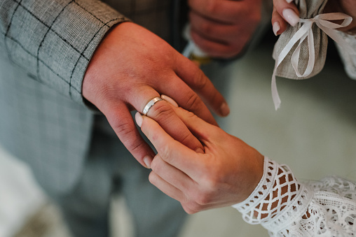 Engagement. The attractive bride wears a golden ring on the finger of the handsome groom. Newlyweds. Ceremony in the church on the wedding day. Hands with wedding rings. Closeup. Top view.