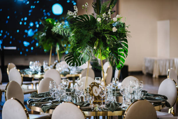 istock Banquet decoration composition flower greenery in hall. Luxury wedding reception. Table setting, setup. Trendy decor for birthday party. Round served tables for guests, plate, glasses, green napkins. 1539436713
