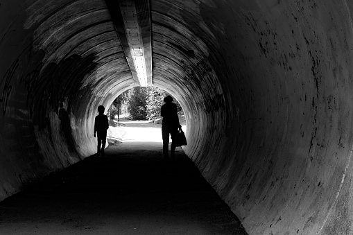 Silhouettes of people in tunnel with dog waiting on the other side.