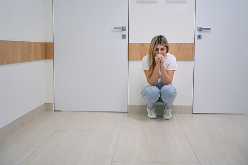 Female blonde woman in jeans is squatting in the hospital corridor, the woman is very upset