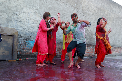 Group of people celebrating Holi festival and dancing on the house floor outdoors. Holi is a popular and significant Hindu festival celebrated as the Festival of Colours, Love and Spring. It celebrates the eternal and divine love of the god Radha and Krishna.