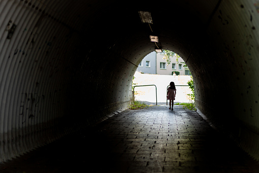 Young woman walking through a tunnel in an urban environment, back view