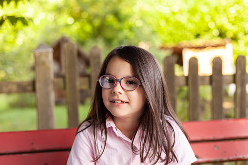 Portrait of a cute little girl wearing glasses sitting on a bench