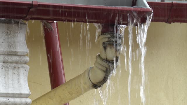 Rain streams flow down from clogged drain pipe along house wall