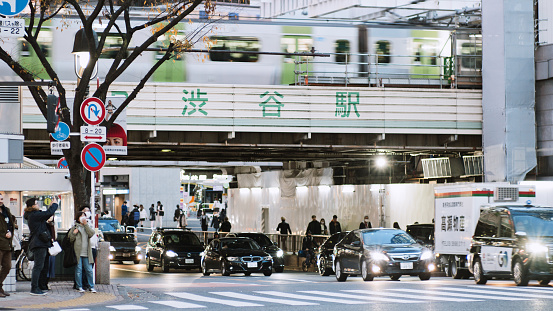 Crowd of Japanese, Asian people, tourist traveler walk cross road at Shibuya scramble crossing in Tokyo Japan. Train transportation on elevated railroad and car driving on road. Asia city life concept