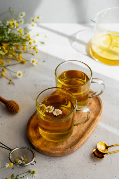 два стакана ромашкового чая на сером столе - chamomile herbal tea chamomile plant tea стоковые фото и изображения