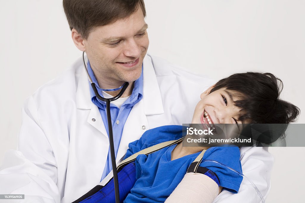 Doctor laughing with injured little boy during checkup Male doctor in early forties holding five year old disabled patient during office visit, laughing together. Child has cerebral palsy. Doctor Stock Photo