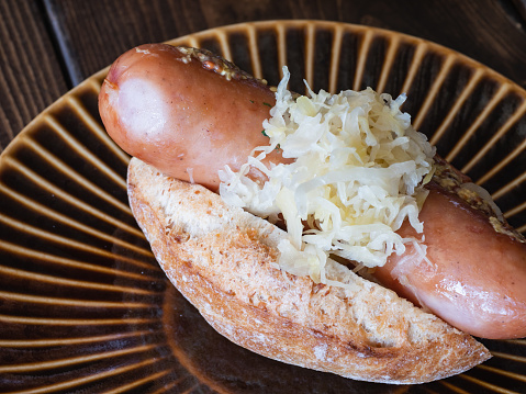 A hot dog with sausage and sauerkraut sandwiched between bread.