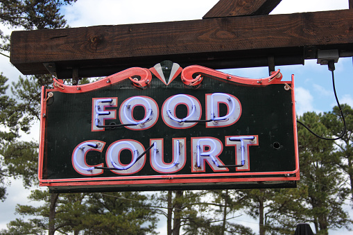 Vintage Purple Neon Food Court Sign Outdoors With Trees in Background