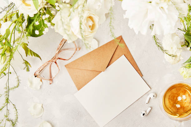 istock Feminine flat lay with crafting pastel paper envelope for greetings, invitation, text among white flowers. Glasses, tea cup and earphones top view 1539573701