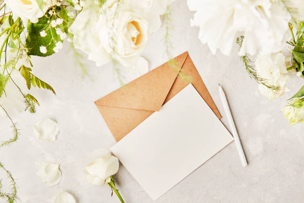 istock Beige paper envelope for invitation, greetings, postcard, text among white flowers. Copy space. Top view. Biophilic interior, cozy home 1539573741