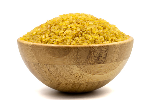 Raw bulgur wheat isolated on white background. Uncooked dried bulgur in wooden bowl