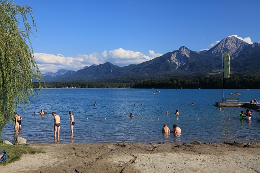 Tourists enjoy the summer at Lake Faak (Faaker See) with view of Karawanks mountain range (Karawanken) in Austria.