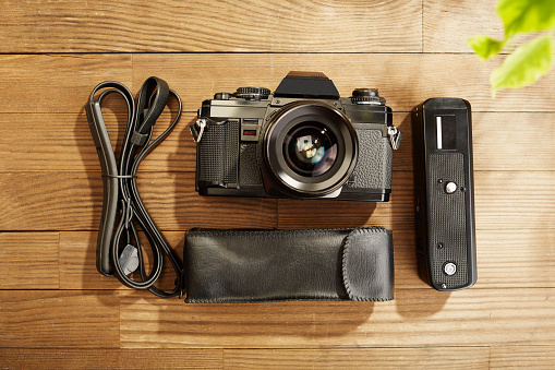 SLR Single-lens reflex professional camera with power winder and neck strap on wooden table