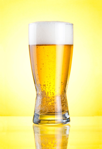 Glass of fresh lager beer close-up with froth over yellow background