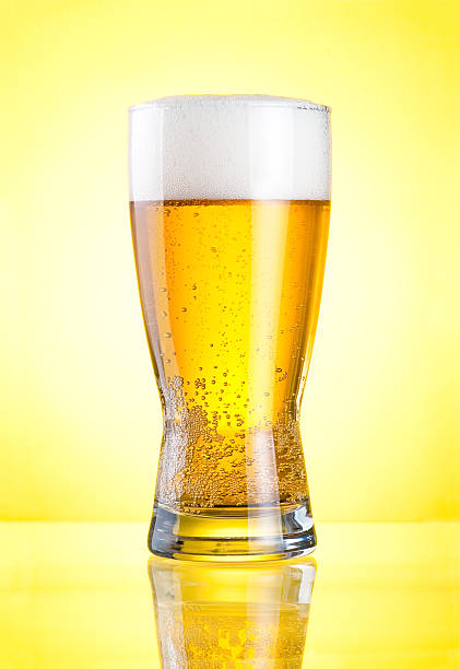 Glass fresh lager beer close-up Glass of fresh lager beer close-up with froth over yellow background unbolted stock pictures, royalty-free photos & images