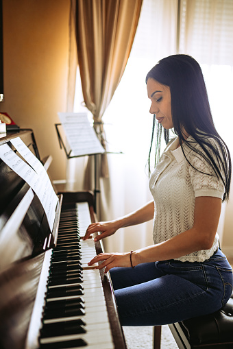 Beautiful young woman playing her piano in her room at home.