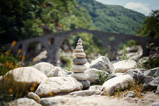Zen stones and pebble rocks stacked on top of each other in balance with the arch of a stone bridge visible at the background