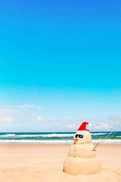Snowman with Santa hat and sunglasses with sand on the beach stock photo