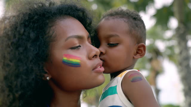 African son kissing his African LGBTQ lesbian mother in pride parade event near seaside, LGBTQ family supporting child adoption
