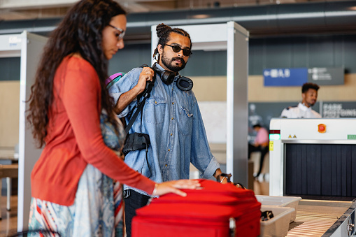 A joyful millennials packs their luggage onto the conveyor belt for security scanning at the airport, making sure their travel experience is seamless and easy.