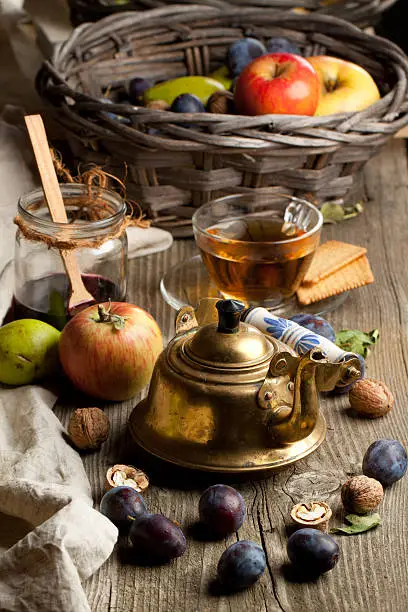 Tea drinking with fresh various fruits, old golden teapot and glass jar of jam in old wooden table