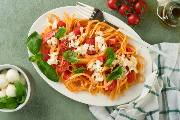istock Salad caprese or pasta spaghetti broken with basil and mozzarella ala caprese on white plate on green rustic wooden background. Traditional Italian cuisine. Italian food concept. Top view. Recipe. 1539716737