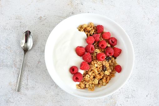 granola with raspberry and yogurt in white plate with spoon top view, copy space