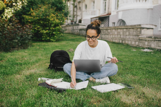 istock Young woman student studying using her books, laptop and notebook, sitting on grass. 1539721436