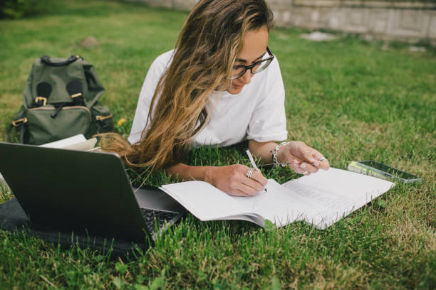 istock Young woman student studying using her books, laptop and notebook, sitting on grass. 1539721946