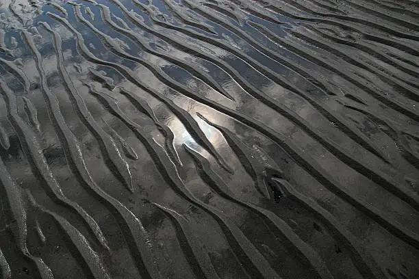 Patterns in beach sand left by water with a reflection of the sun.