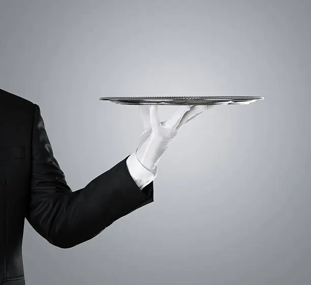 Waiter holding empty silver tray over gray background with copy space