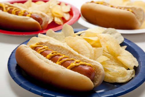 Several hot dogs and potato chips on colored plates at a picnic