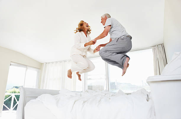 Having fun at any age! Excited senior couple jumping on their bed at home old man pajamas photos stock pictures, royalty-free photos & images