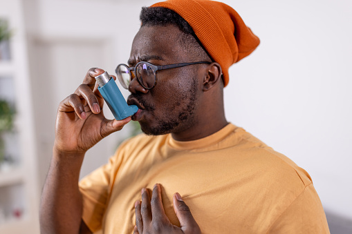 Exhibiting resilience in the face of asthma challenges, the young African American man conquers each breath with his inhaler at home, demonstrating his ability to thrive and flourish despite the obstacles