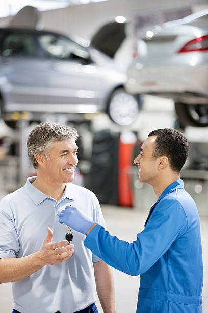 souriant mécanicien de confier les clés de voiture à homme de réparation automobile - auto repair shop customer auto mechanic mechanic photos et images de collection