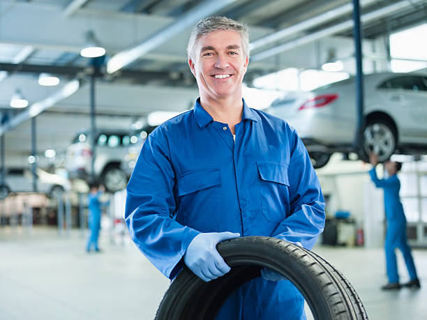retrato do mecânico sorridente segurando pneus na oficina de automóvel - repairing auto repair shop service technician - fotografias e filmes do acervo