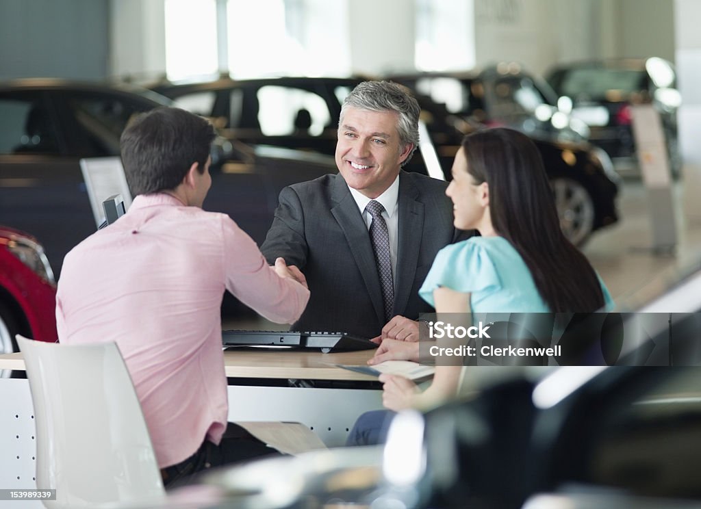Sorridente venditore stringe la mano con coppia alla reception - Foto stock royalty-free di Concessionaria automobilistica