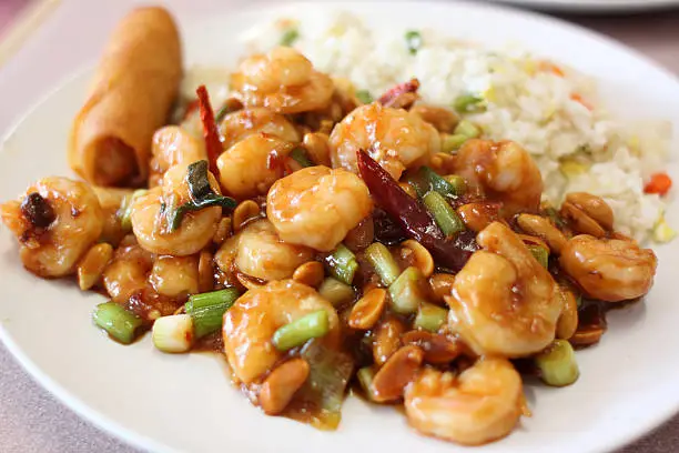 Plate of kung pao shrimp with rice and egg roll at a Chinese restaurant.