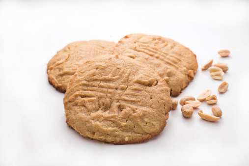 Three jumbo peanut butter cookies on a white background with peanuts accented on the side. Selective focus on front cookie and peanuts